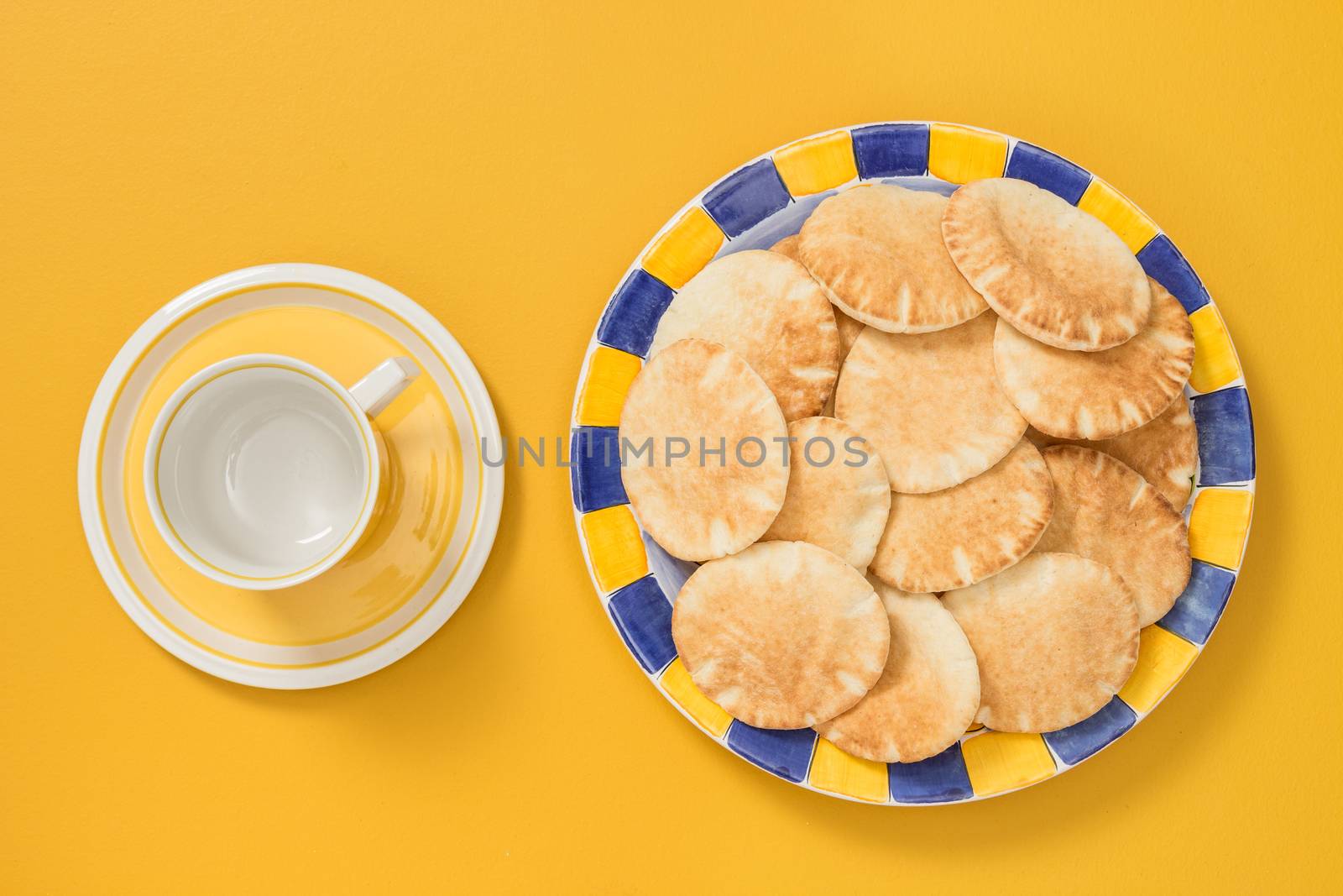 Teacup and plate with pita bread on yellow background by anikasalsera