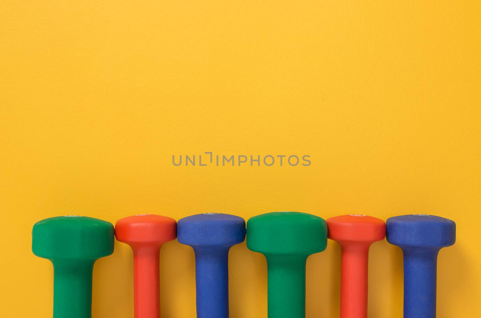 Multicolored dumbbells on bright yellow background by anikasalsera
