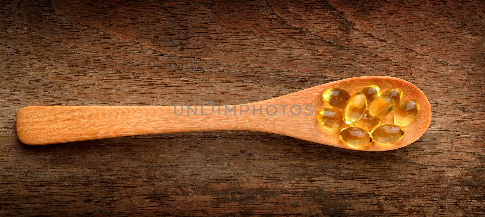 Fish oil capsules in a spoon on wood 