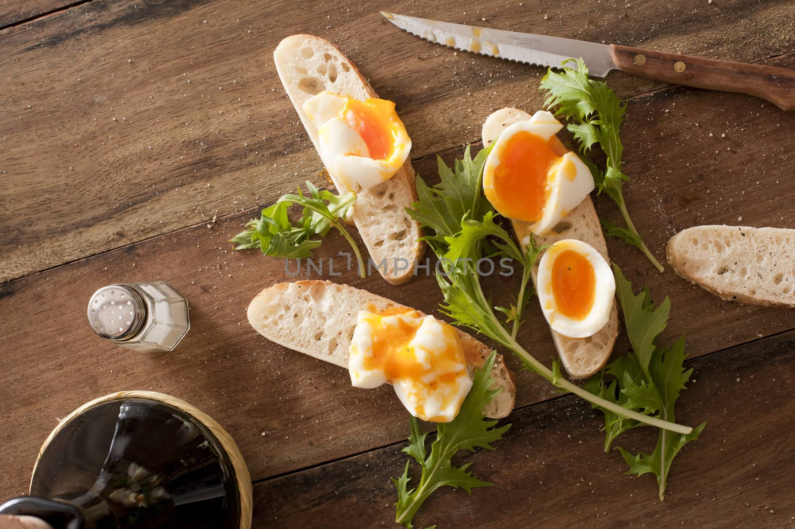 Bread soldiers with soft-boiled eggs, thin strips of toasts with greens and knife over wooden table
