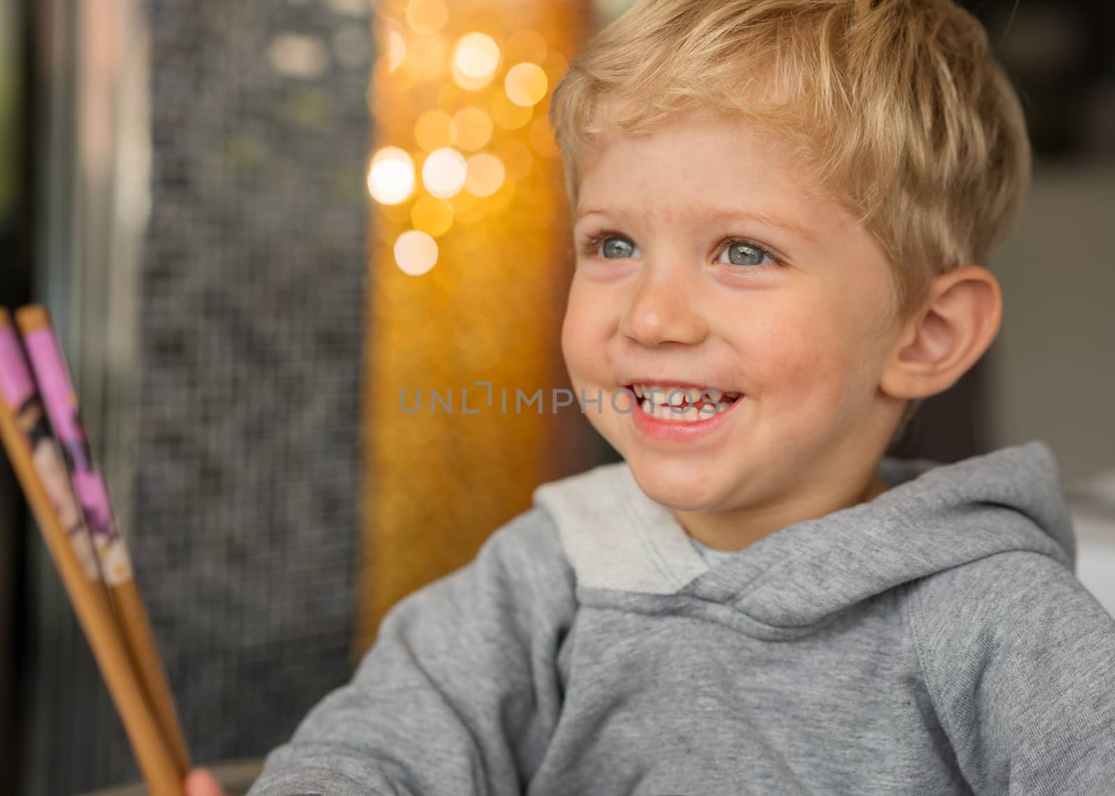Baby boy sitting in high chair plays with chopsticks and smiling happiness at chinese restaurant.Natural light background with nice bokeh,horizontal photo.