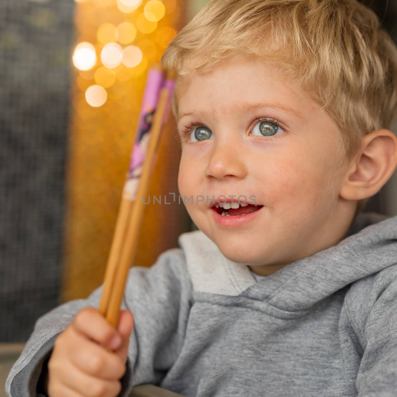 Baby boy sitting in high chair plays with chopsticks and smiling happiness at chinese restaurant.Natural light background with nice bokeh,horizontal photo,close up.