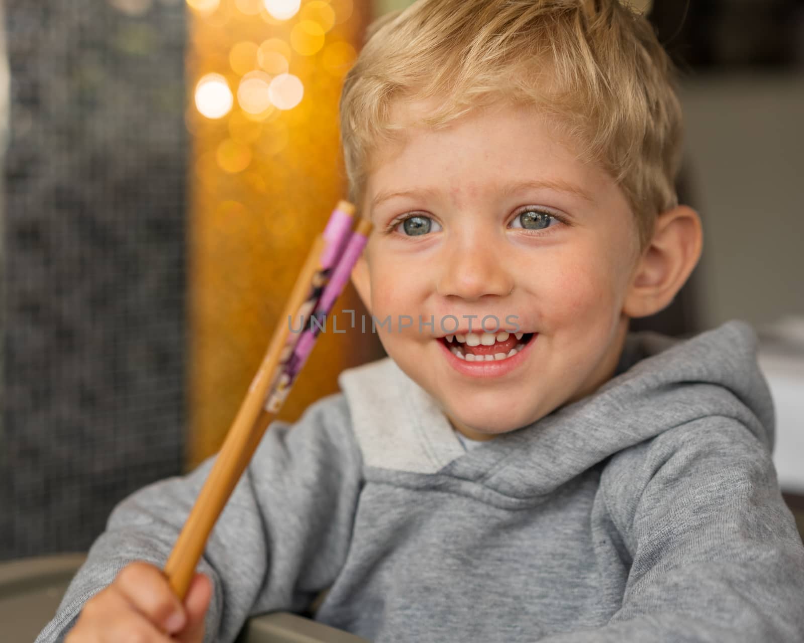 Baby boy sitting in high chair plays with chopsticks and smiling happiness at chinese restaurant.Natural light background with nice bokeh,horizontal photo.