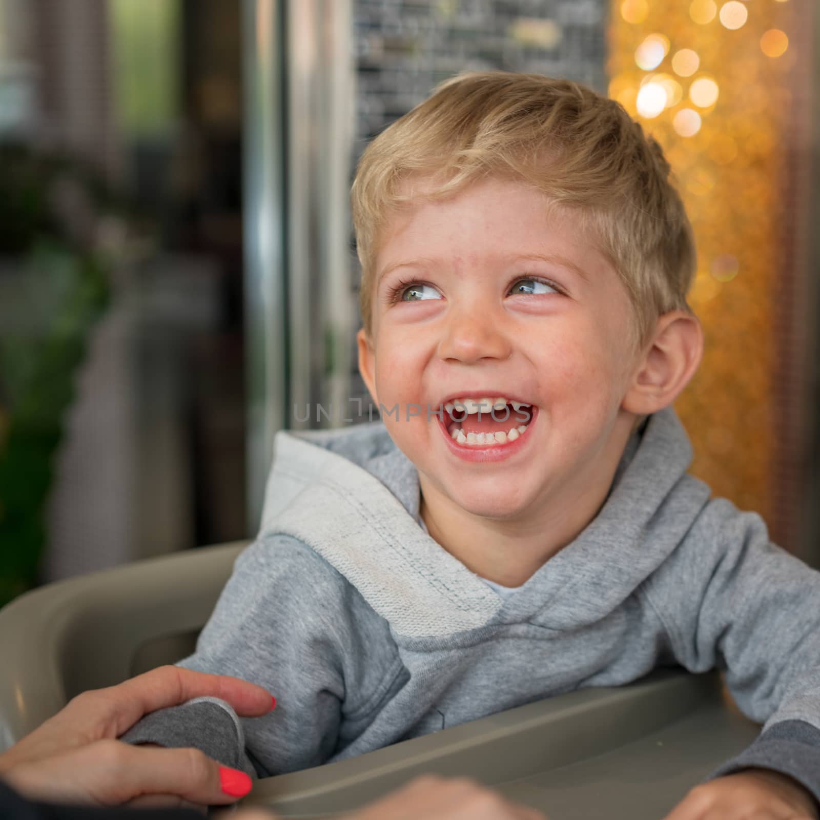 Baby boy sitting in high chair plays and smiling happiness at chinese restaurant.Natural light background with nice bokeh,horizontal photo.