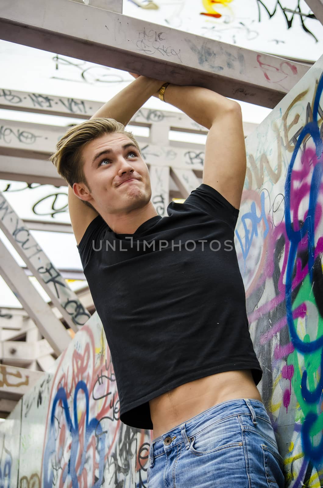 Attractive blue eyed, blond young man in black t-shirt hanging from concrete structure