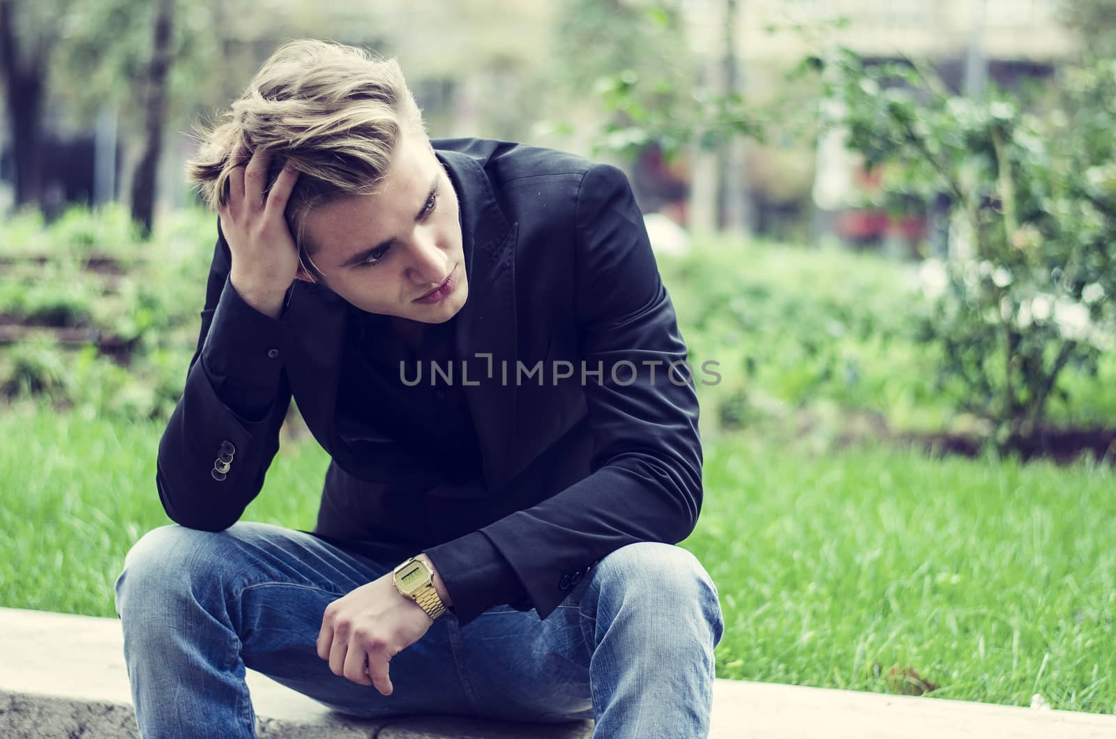 Close up Disappointed Young White Man Sitting at Street Side with Grassy Landscape at the Background