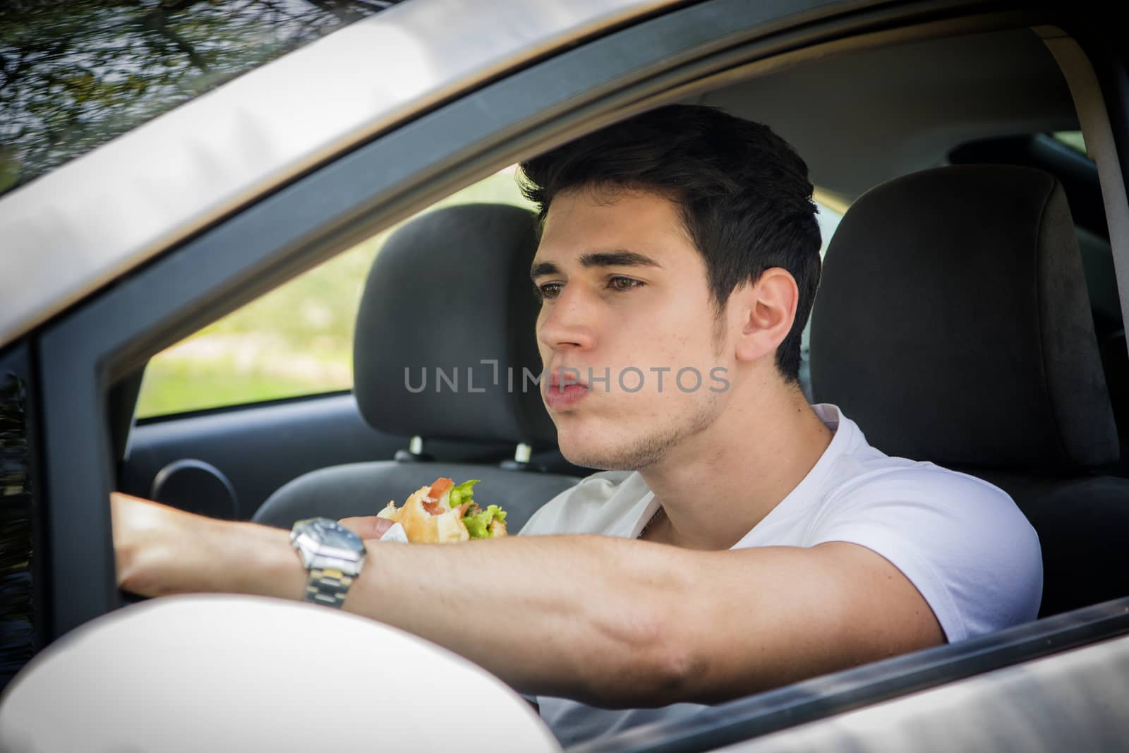 Young handsome man driving his car while eating food in the traffic