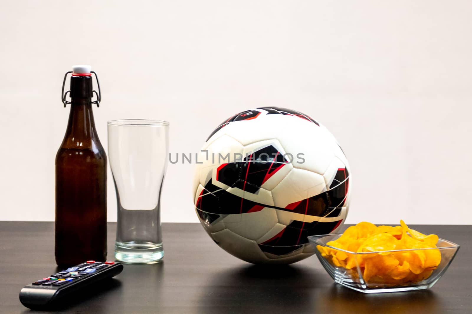 People prepared to watch football on TV with beer. There's beer on the table, ball, TV remote, snacks. Craft beer. Light background.