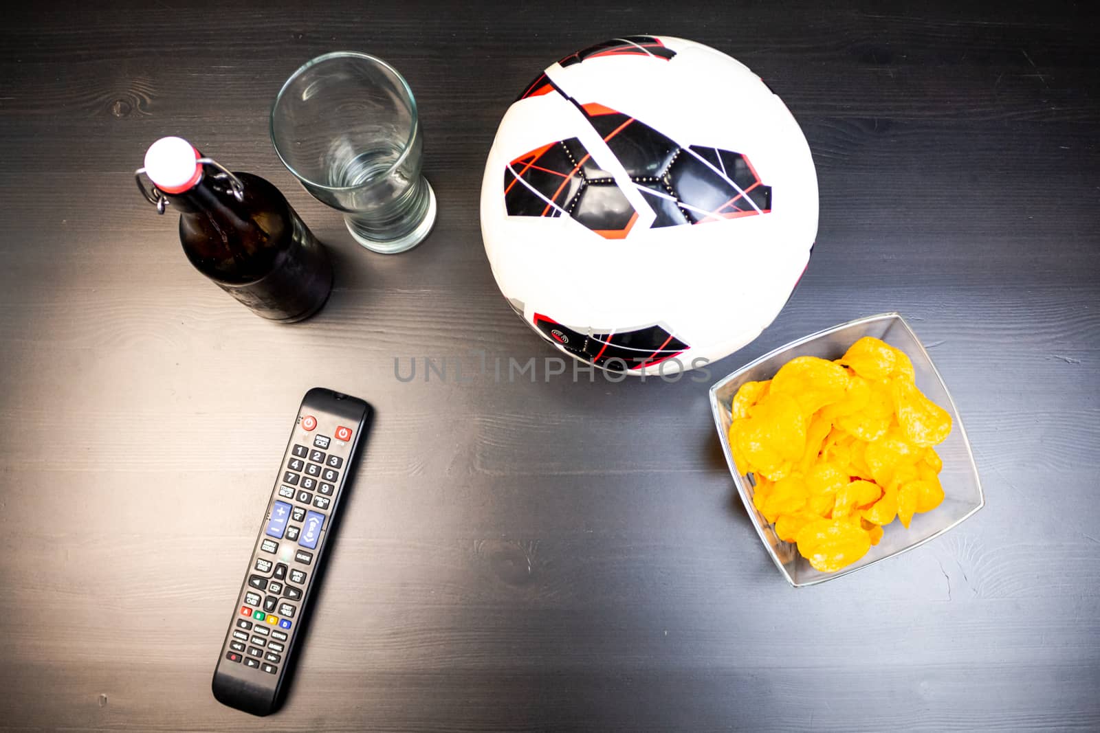 People prepared to watch football on TV with beer. There's beer on the table, ball, TV remote, snacks. Craft beer. Light background. The view from the top.