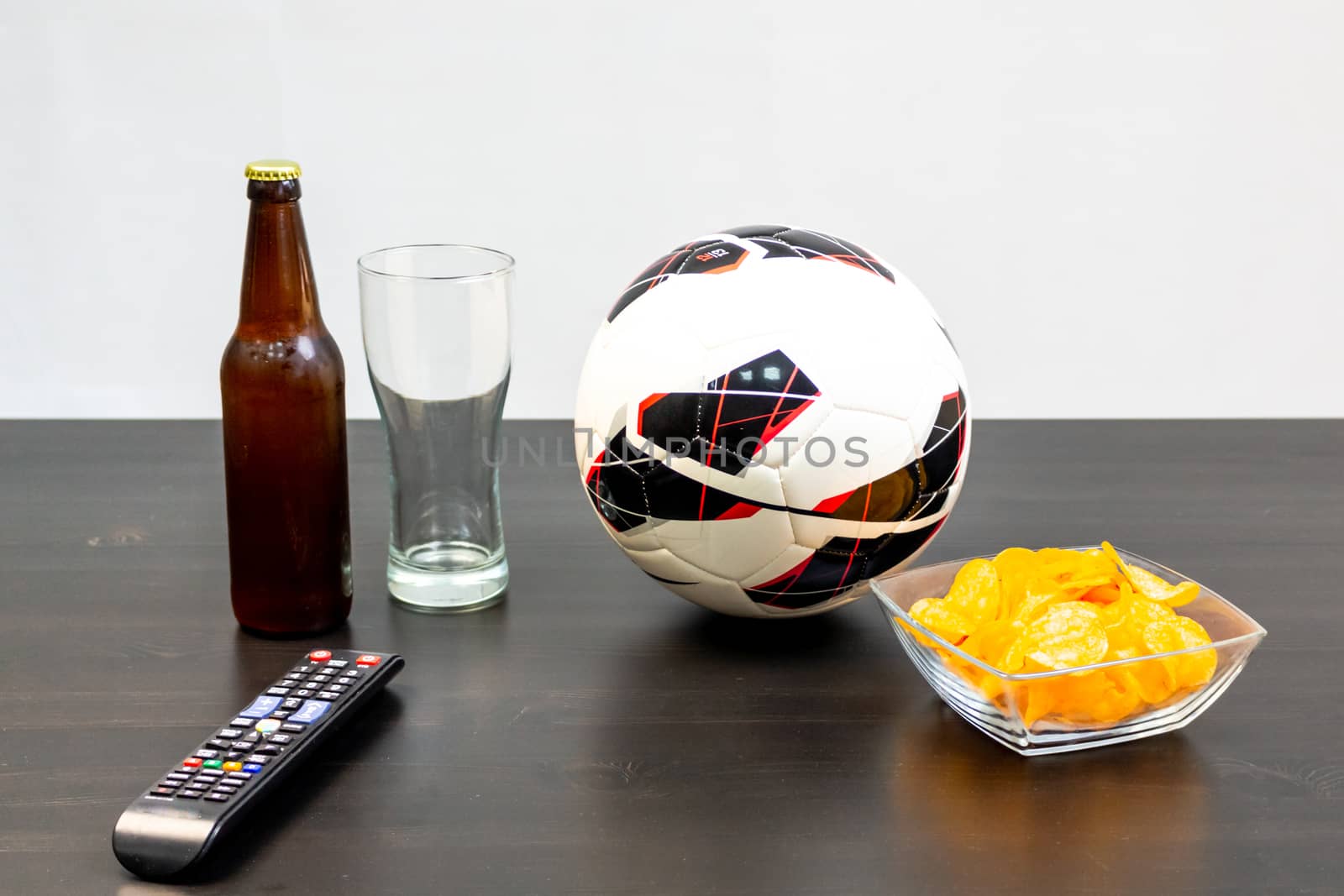 People prepared to watch football on TV with beer. There's beer on the table, ball, TV remote, snacks. Craft beer. Light background.