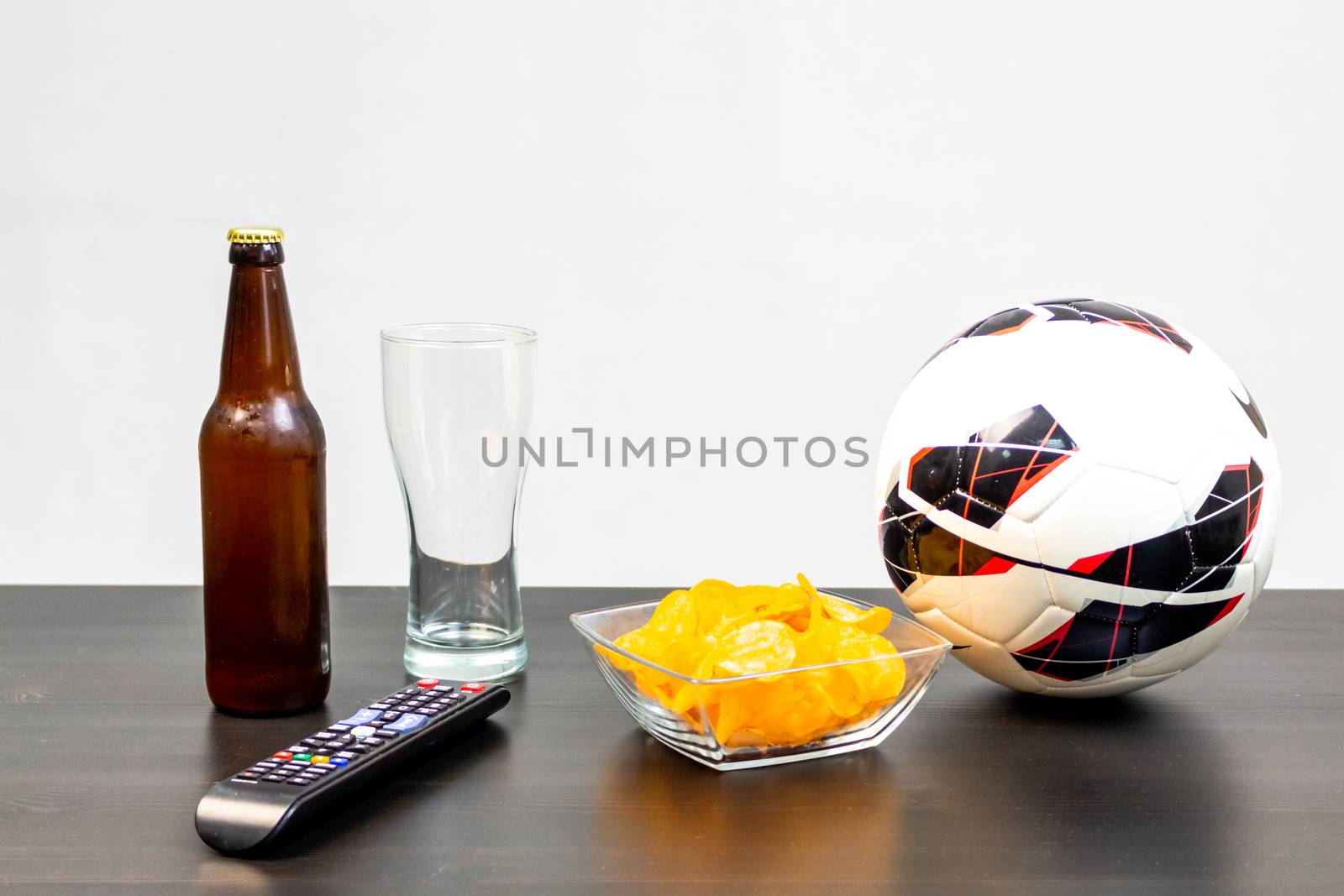 People prepared to watch football on TV with beer. There's beer on the table, ball, TV remote, snacks. Craft beer. Light background.