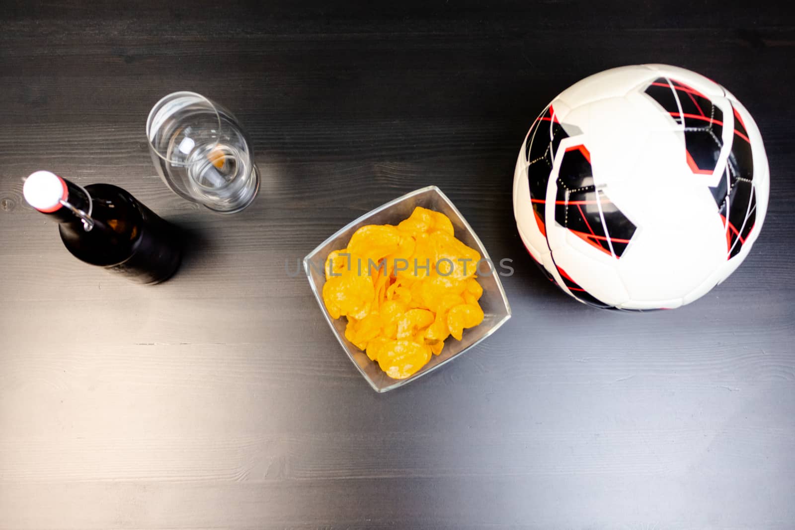 People prepared to watch football on TV with beer. There's beer on the table, ball, TV remote, snacks. Craft beer. Light background. The view from the top.