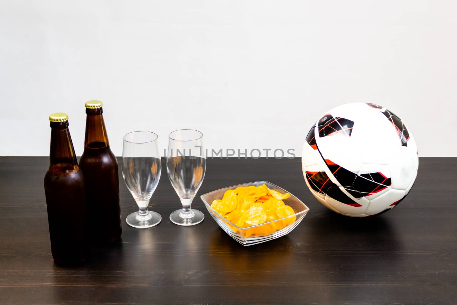 People prepared to watch football on TV with beer. There's beer on the table, ball, TV remote, snacks. Craft beer. Light background.