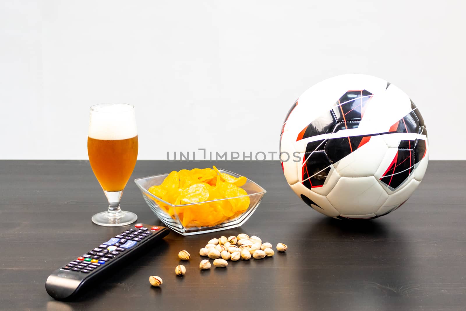 People prepared to watch football on TV with beer. There's beer on the table, ball, TV remote, snacks. Craft beer. Light background.