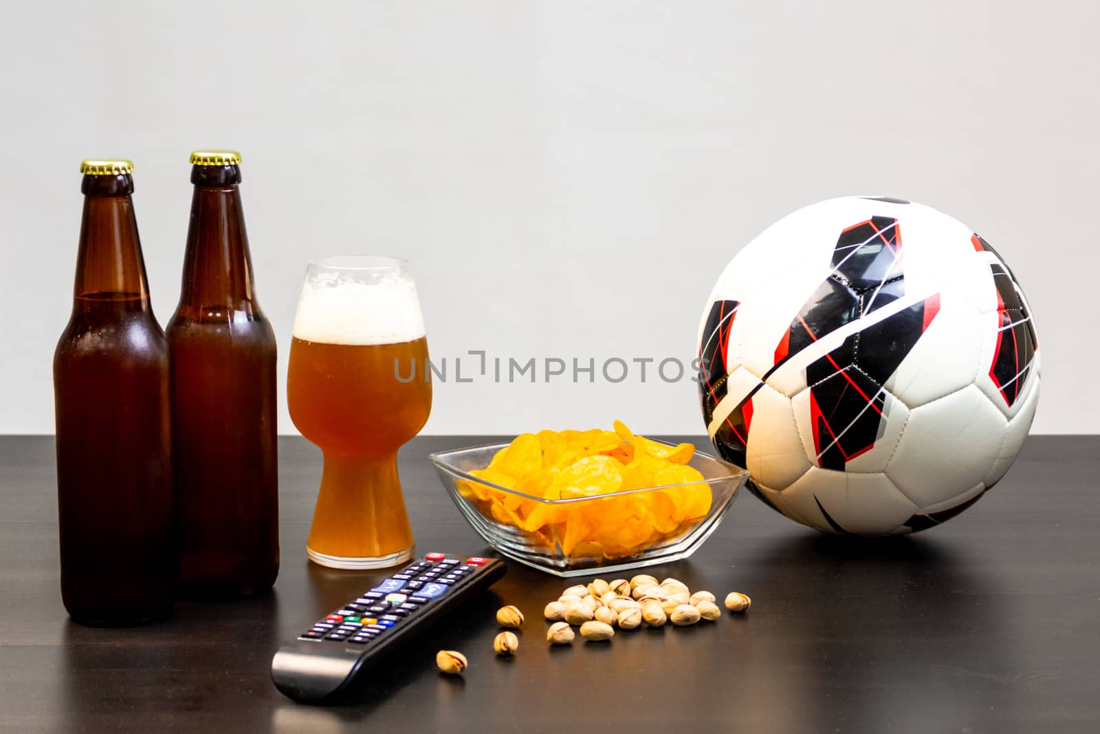 People prepared to watch football on TV with beer. There's beer on the table, ball, TV remote, snacks. Craft beer. Light background.