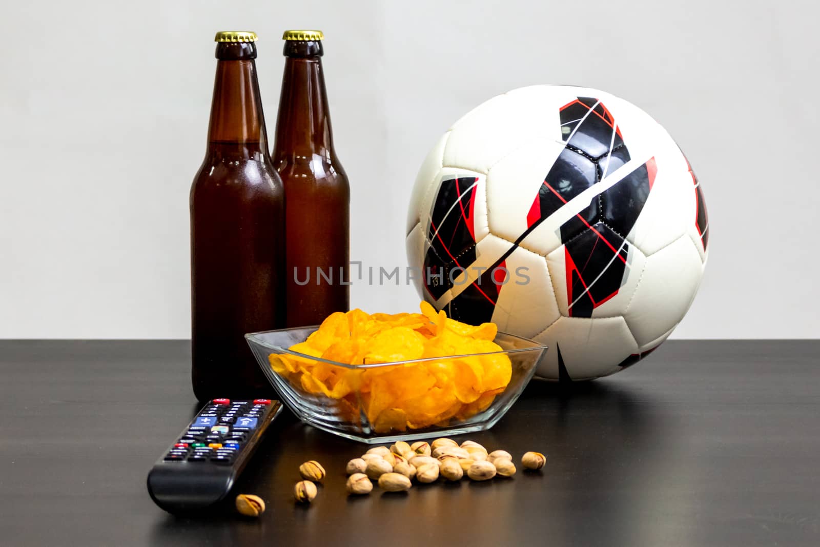 People prepared to watch football on TV with beer. There's beer on the table, ball, TV remote, snacks. Craft beer. Light background.