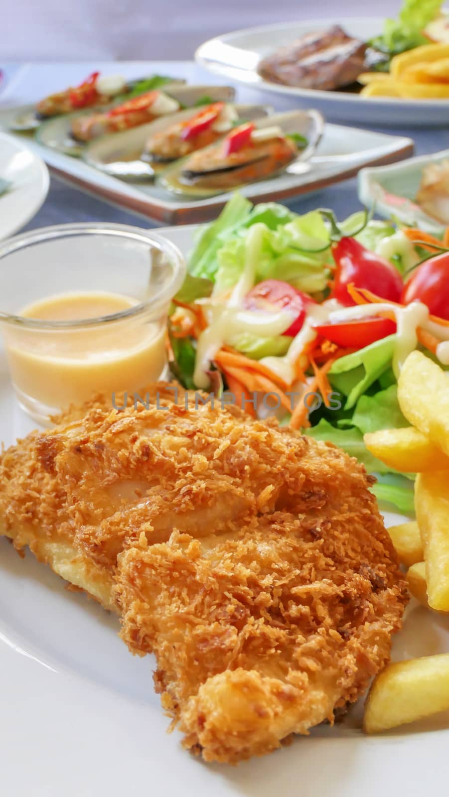 Deep fried fish steak served with french fries and fresh vegetables on plate , And  full of food on table