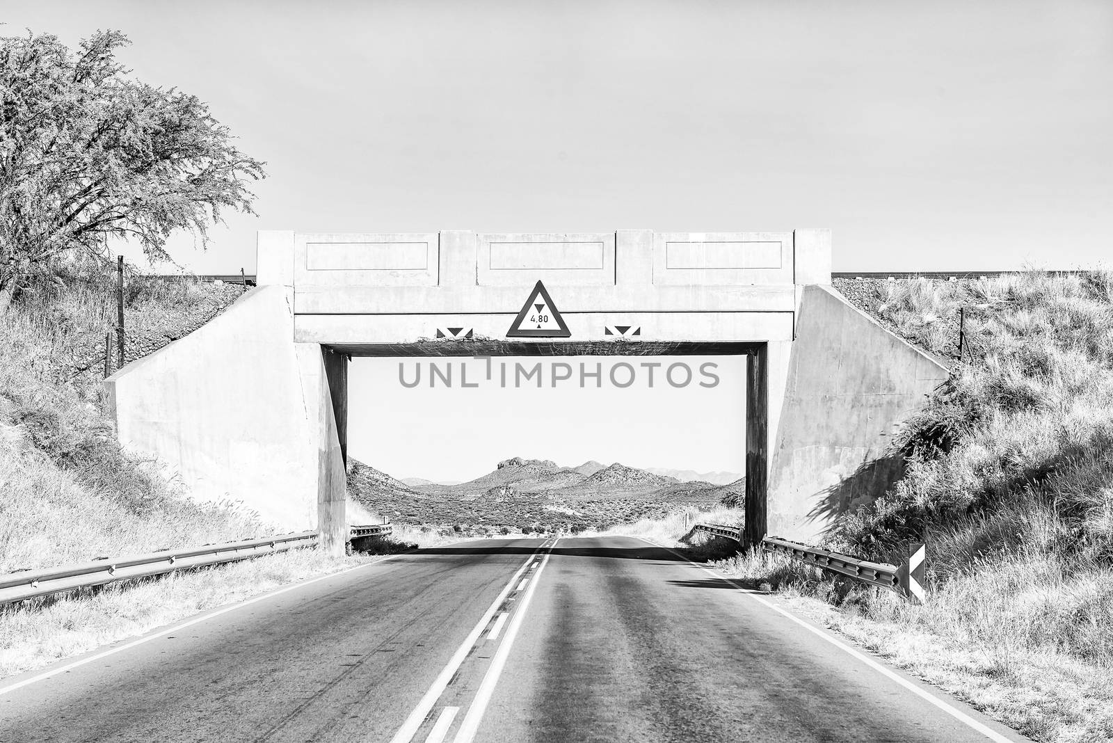A monochrome view of a railway bridge over the B1-road frames a mountain scene south of Windhoek, the capital city of Namibia