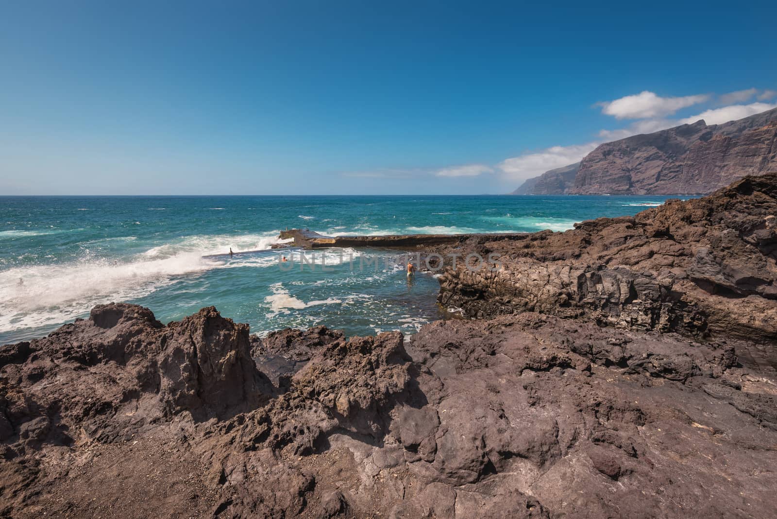 Unidentifiable Tourist swimming in coastline landscape in Puerto Santiago, Tenerife, Spain.