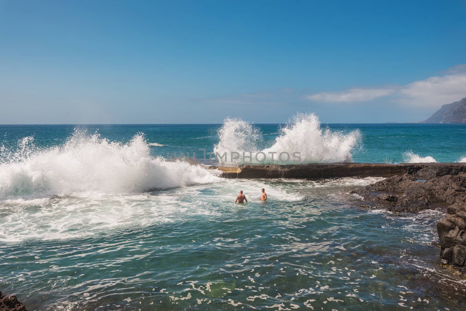 Unidentifiable Tourist swimming in coastline landscape in Puerto Santiago, Tenerife, Spain.