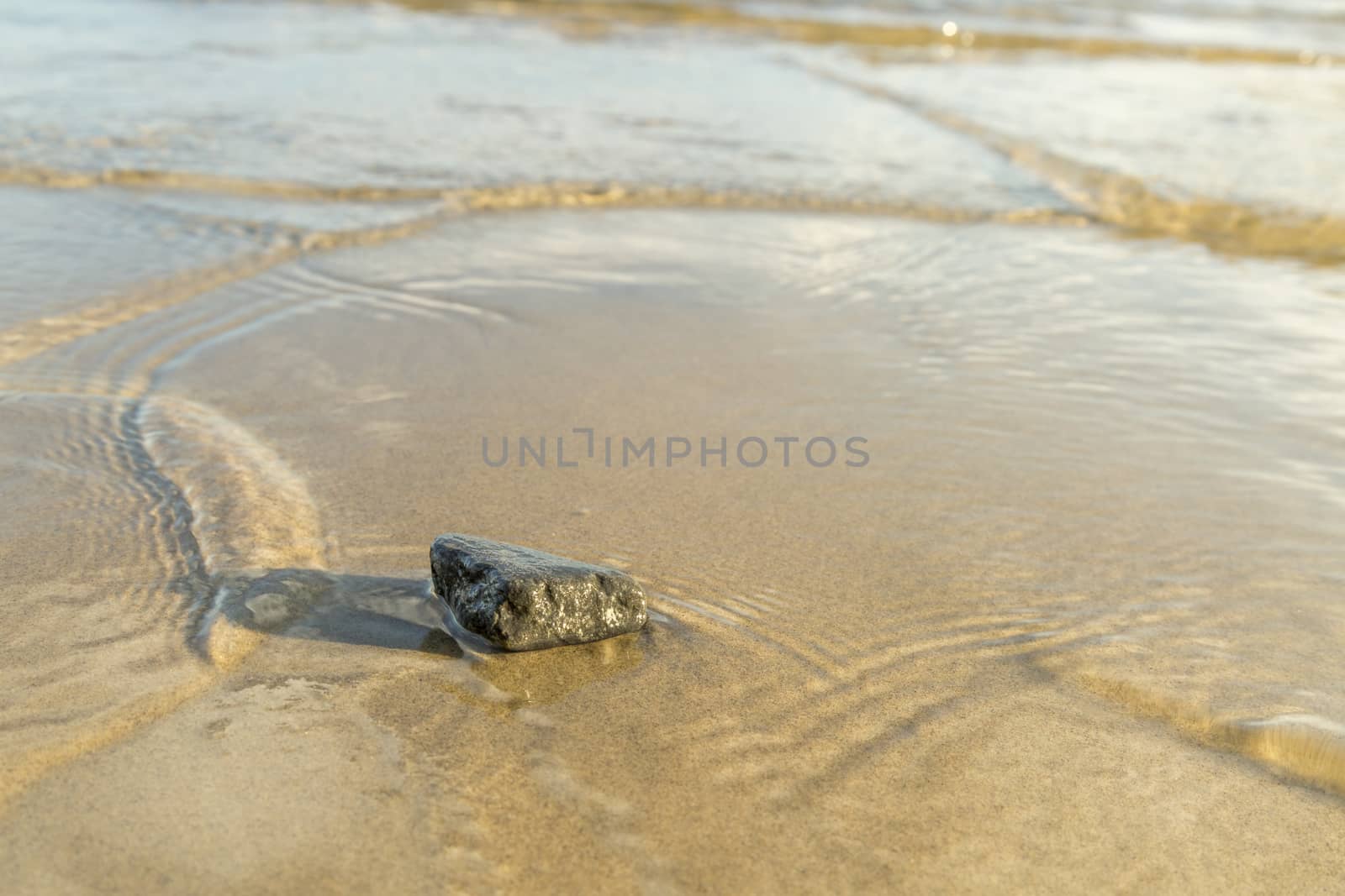 Stone in Sand with Water Ripples close up.