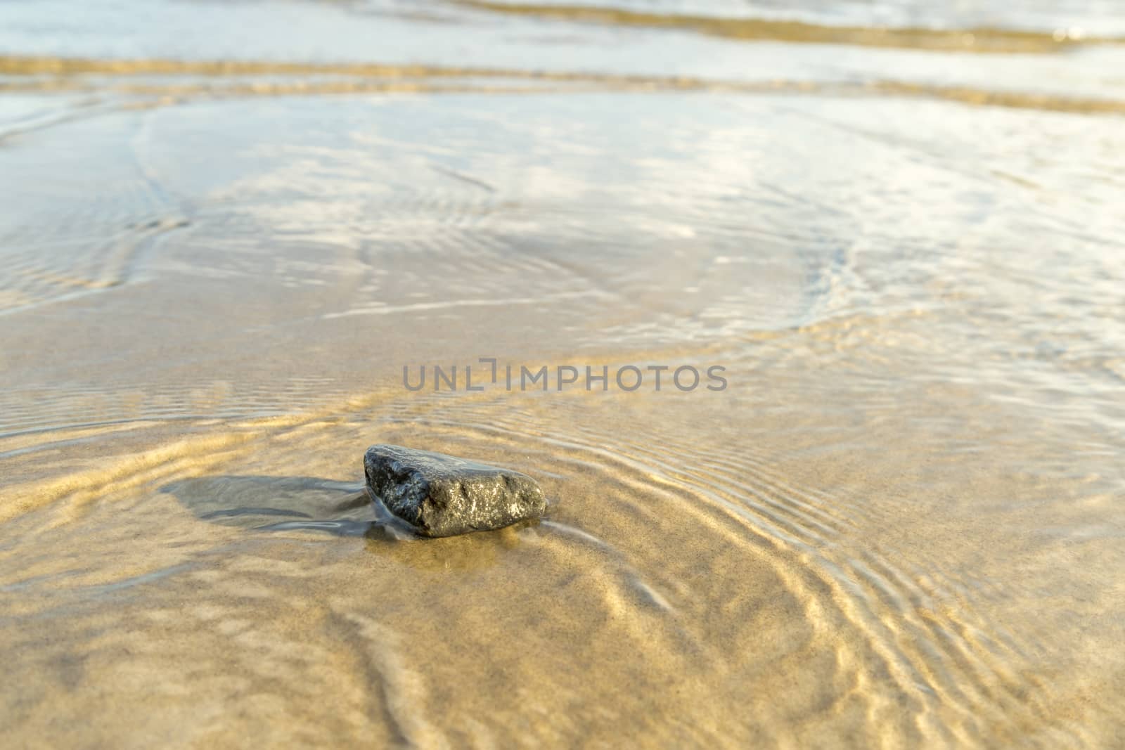 Stone in Sand with Water Ripples close up.