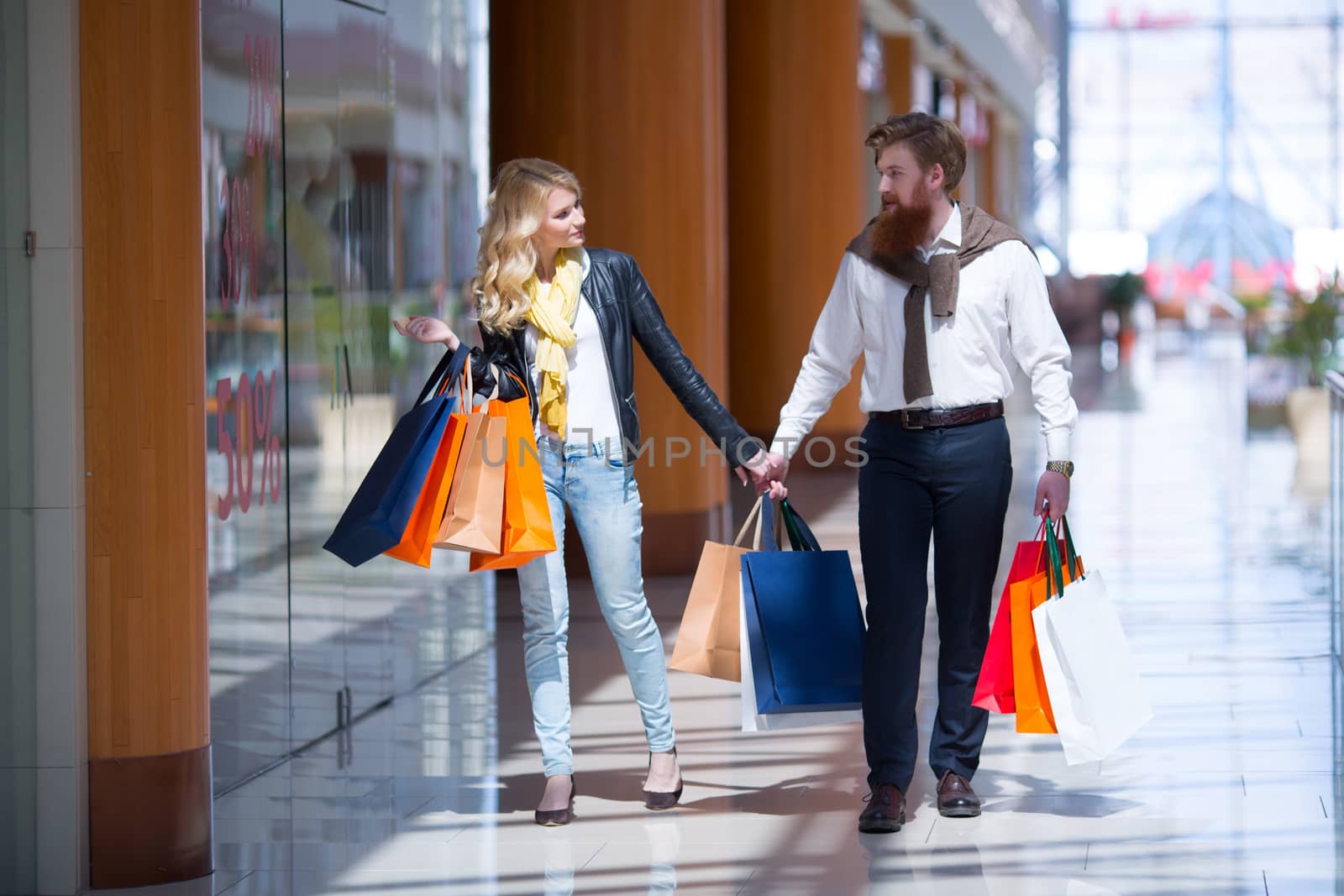 Happy beautiful young couple with shopping bags walking holding hands in mall