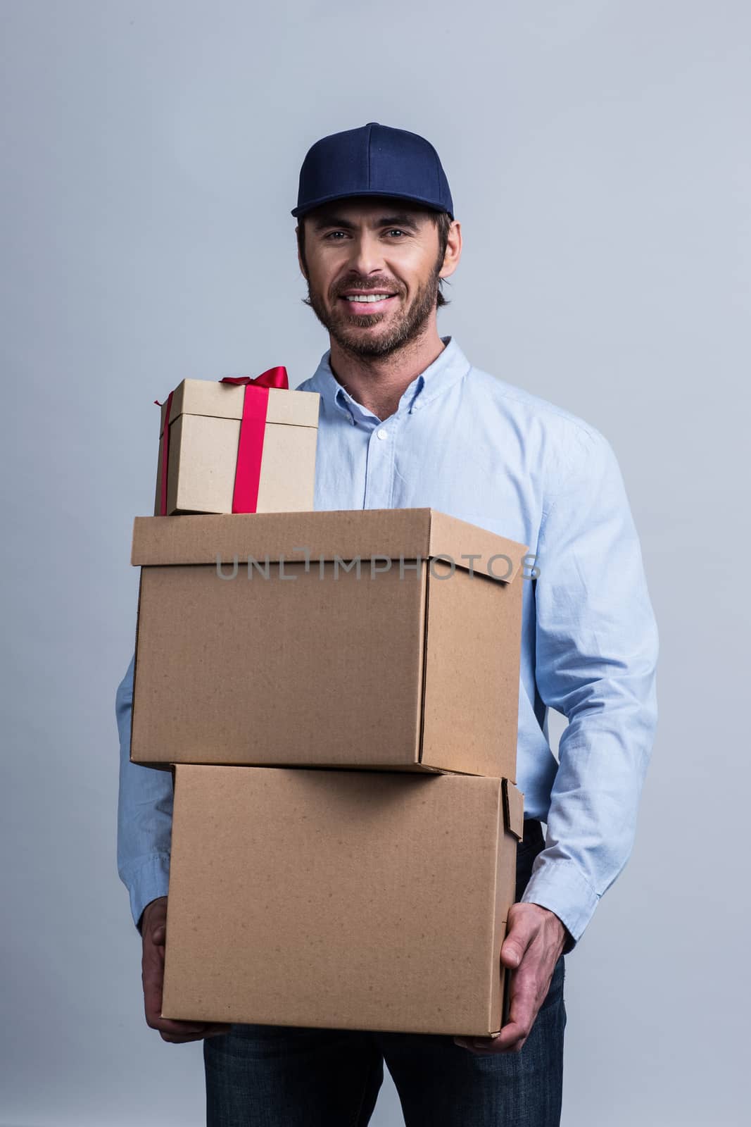 Happy smiling delivery man in uniform cap holding box stack