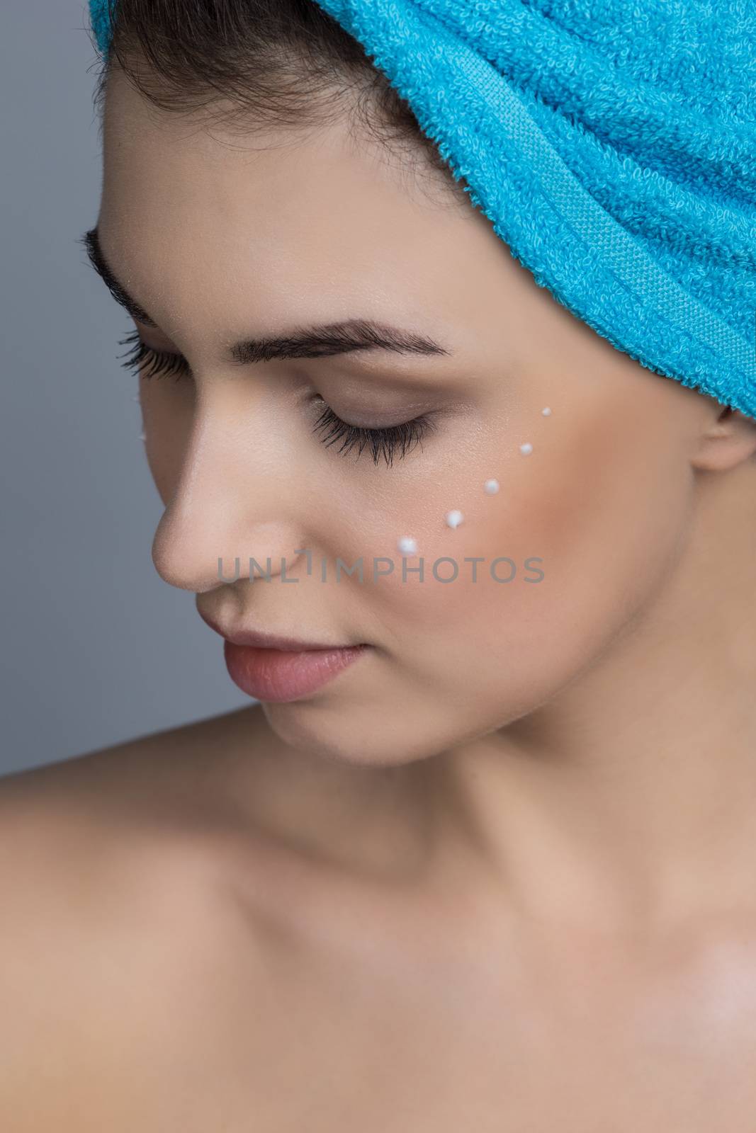 Beautiful woman with towel on head applying creme after shower