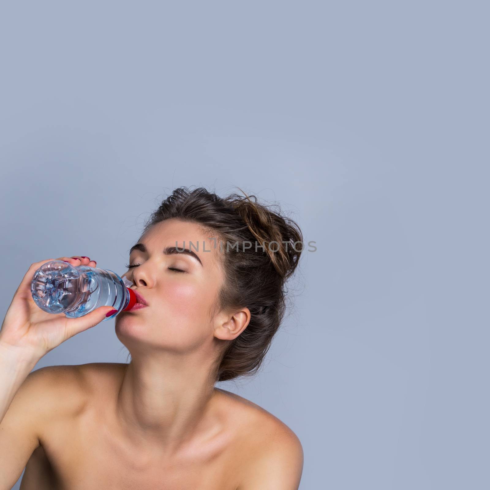 Portrait of a beautiful happy woman with perfect skin drinking water from bottle