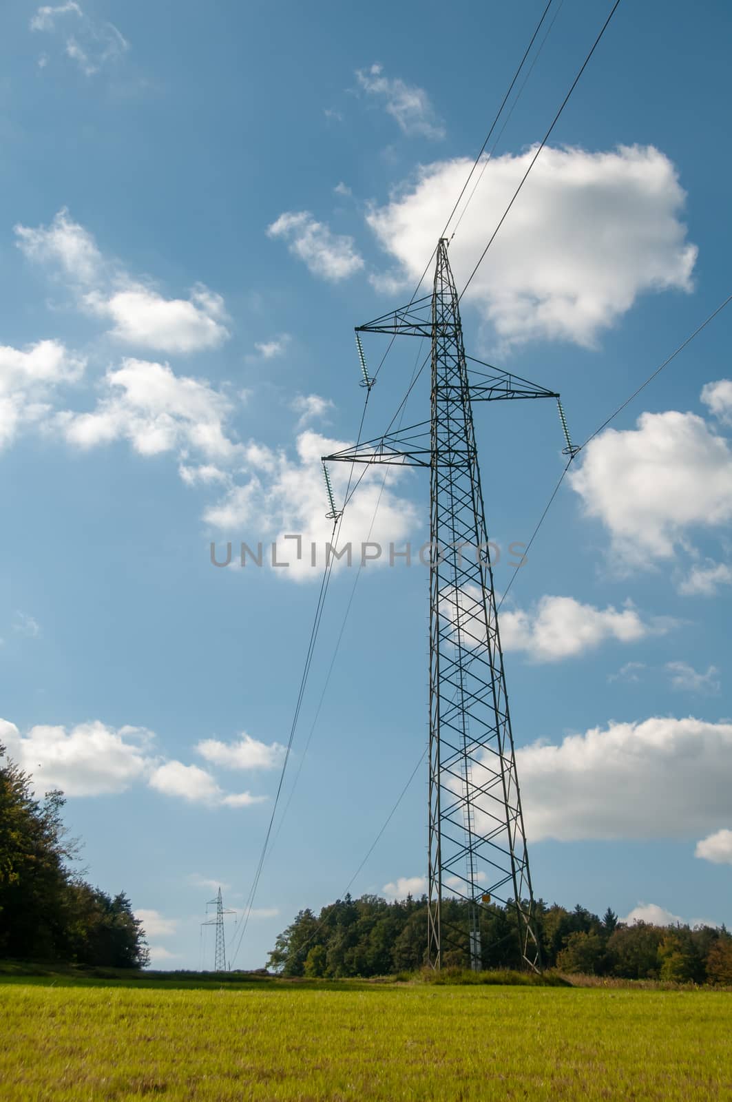 High voltage lines and power pylons innatural landscape on blue sky with puffy clouds, cology concept