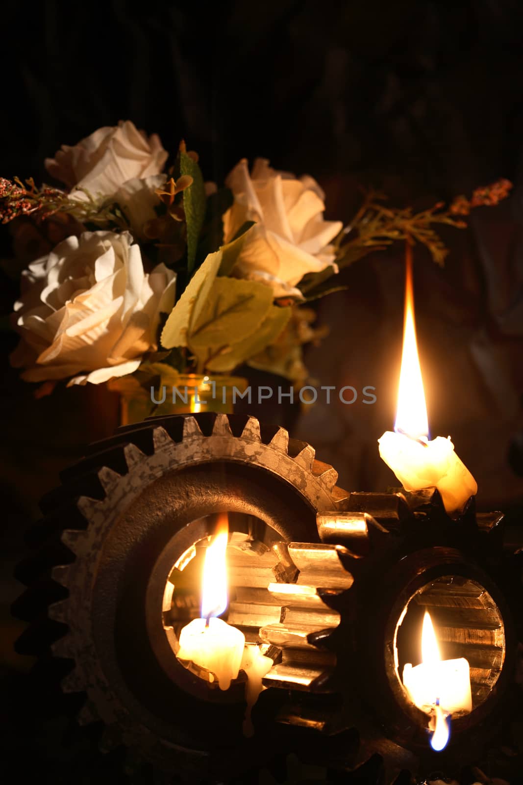 Lighting candles on old gears near roses against dark background