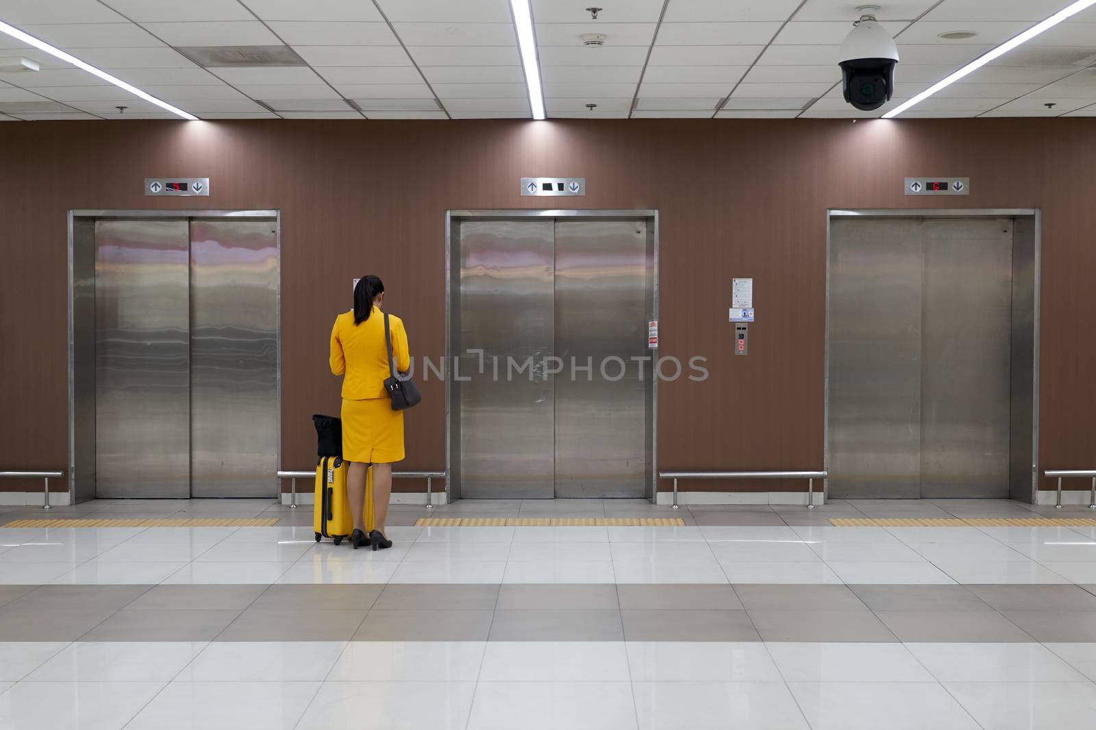 Air hostess with yellow uniform is checking her flight schedule and waiting elevator at the international airport terminal with copy space.