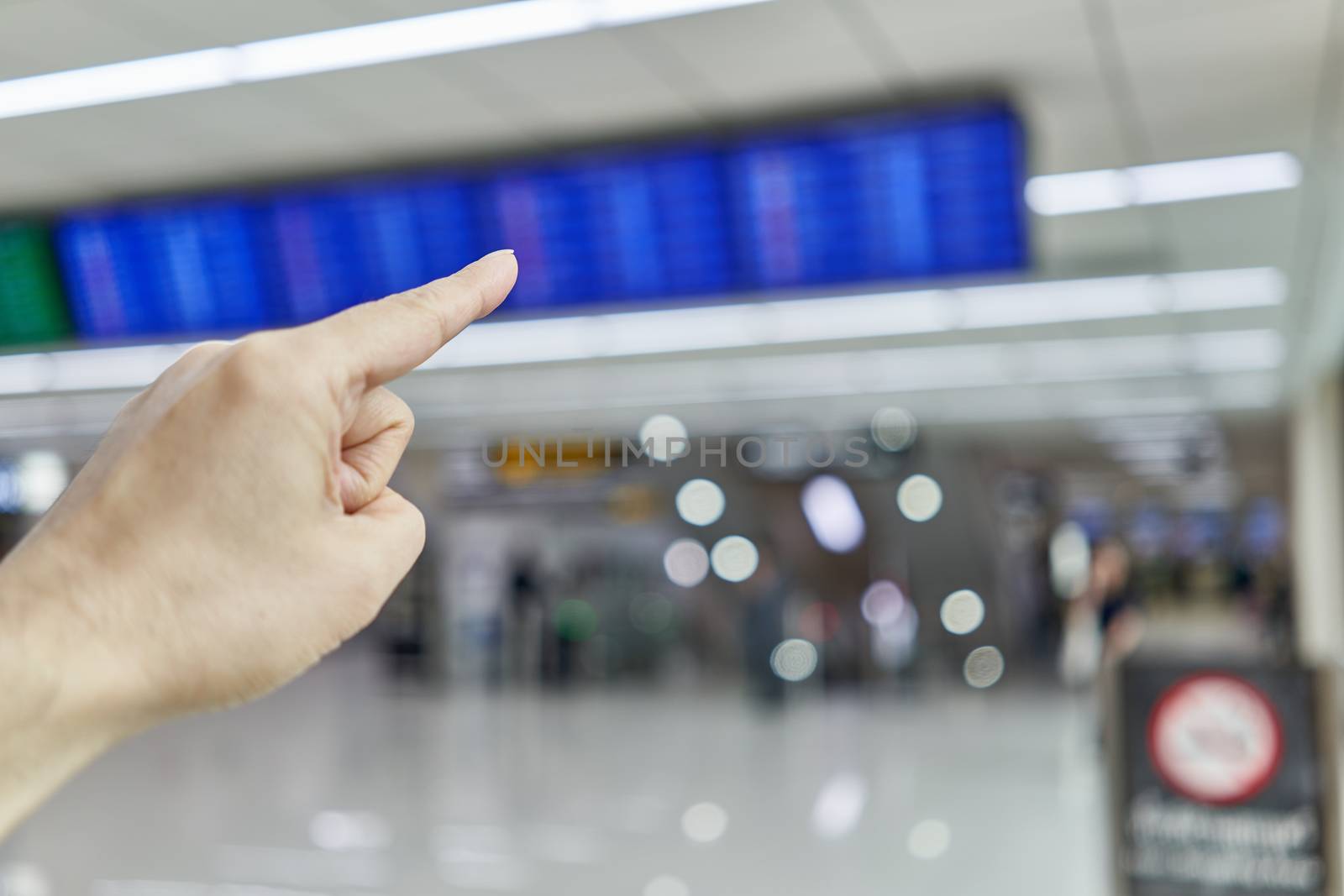 Finger of man is pointing at blur flight schedule for check timetable to departure in non smoking area at international airport terminal with copy space.