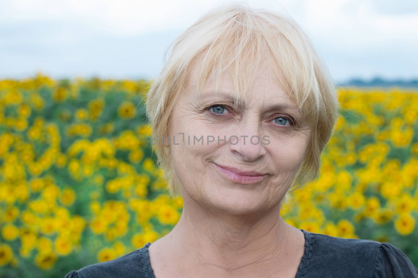 Headshot portrait of smiling aged retired blond white woman with direct sight of green blue eyes looking into camera