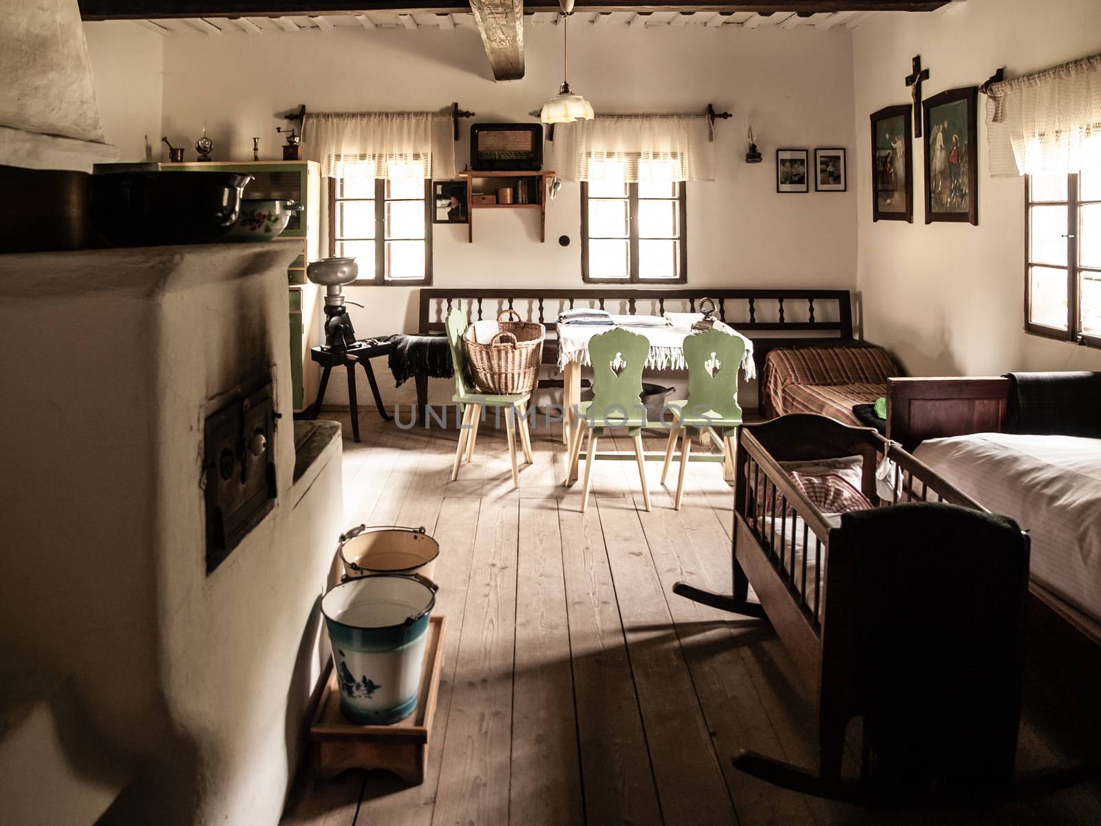 Vintage room with bed, cradle, furnace, table and chairs in old rural house. Sepia style image.