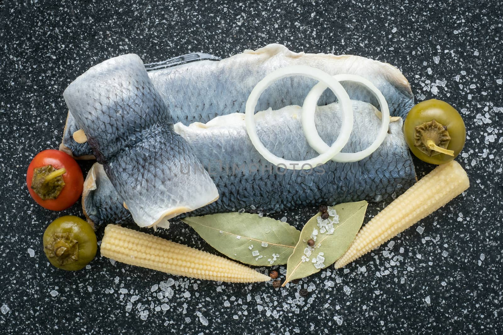 Saltwater marinated fish, cold appetizer. Herring fillet marinated on black cutting board