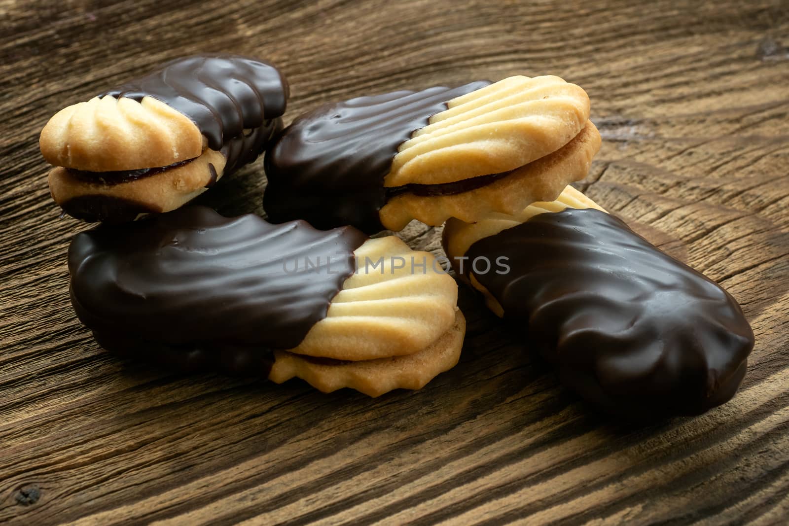 Cookies on wooden table. Biscuits with filling on wooden desk. Sweet cookies dipped in chocolate.