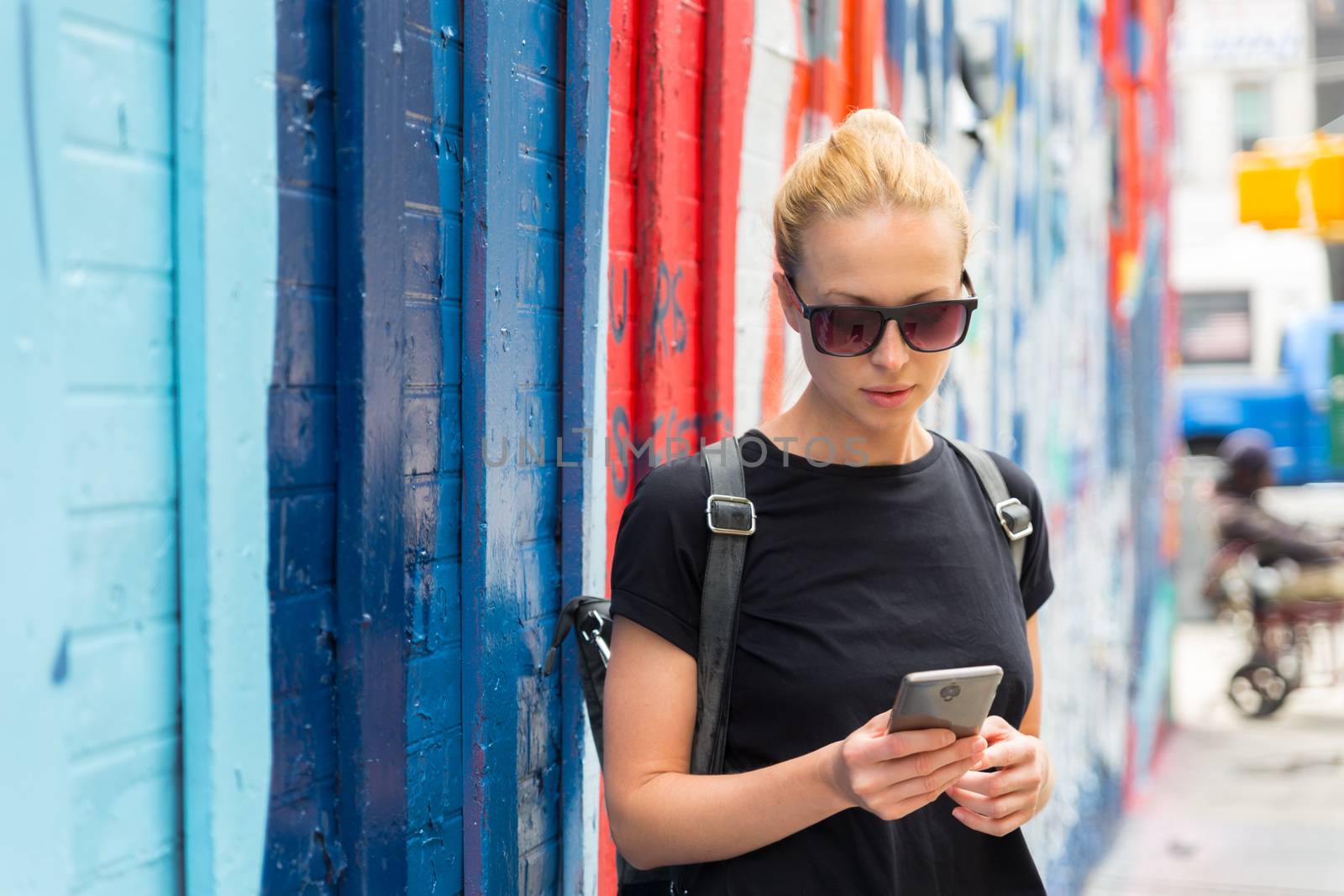 Closeup of female hipster with smart phone. Woman using smartphone against colorful graffiti wall in East Village, New York city, USA.