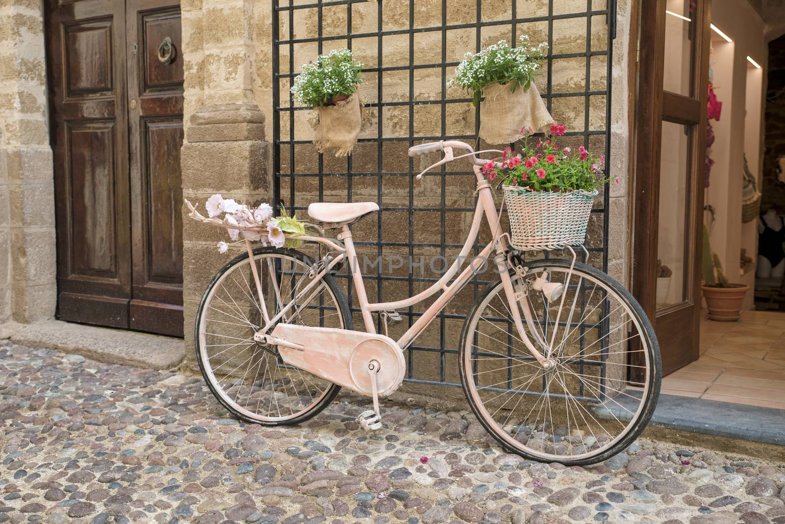 pink painted ladies bike with flowers in street with old doors and stones on sardinia island