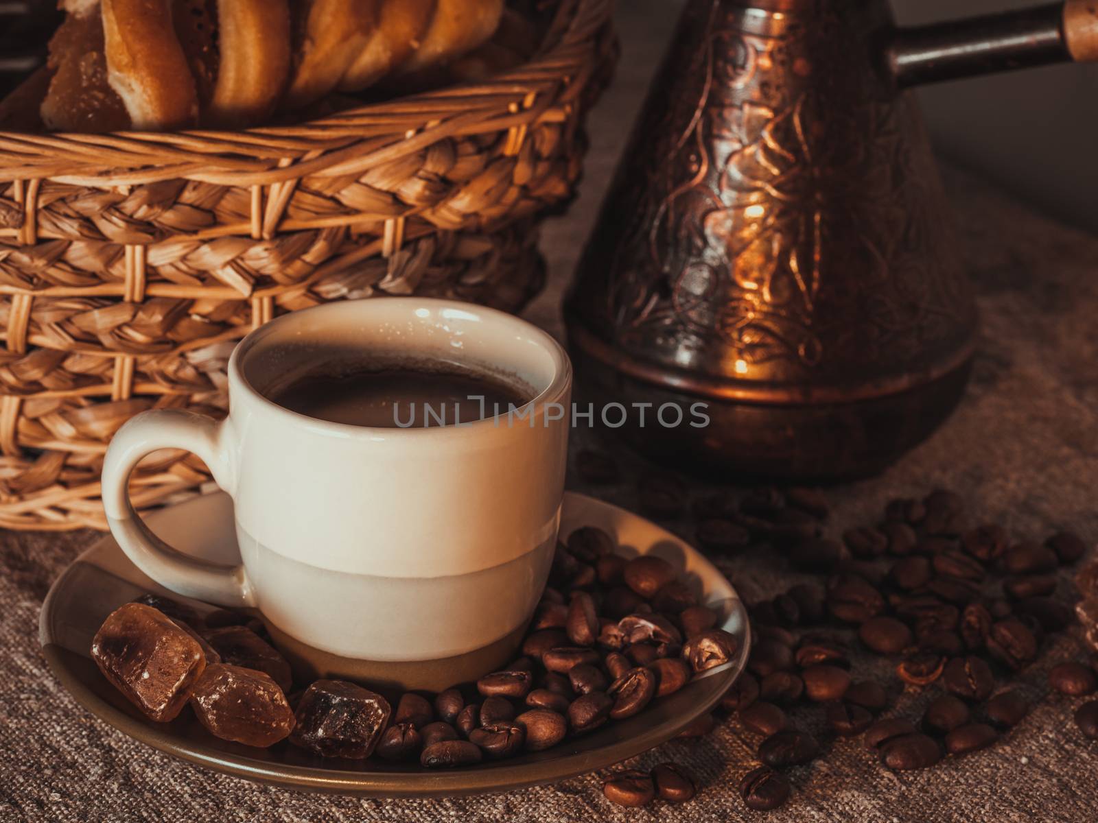A cup of coffee on textile with coffee beans, dark candy sugar, pots, basket and cake