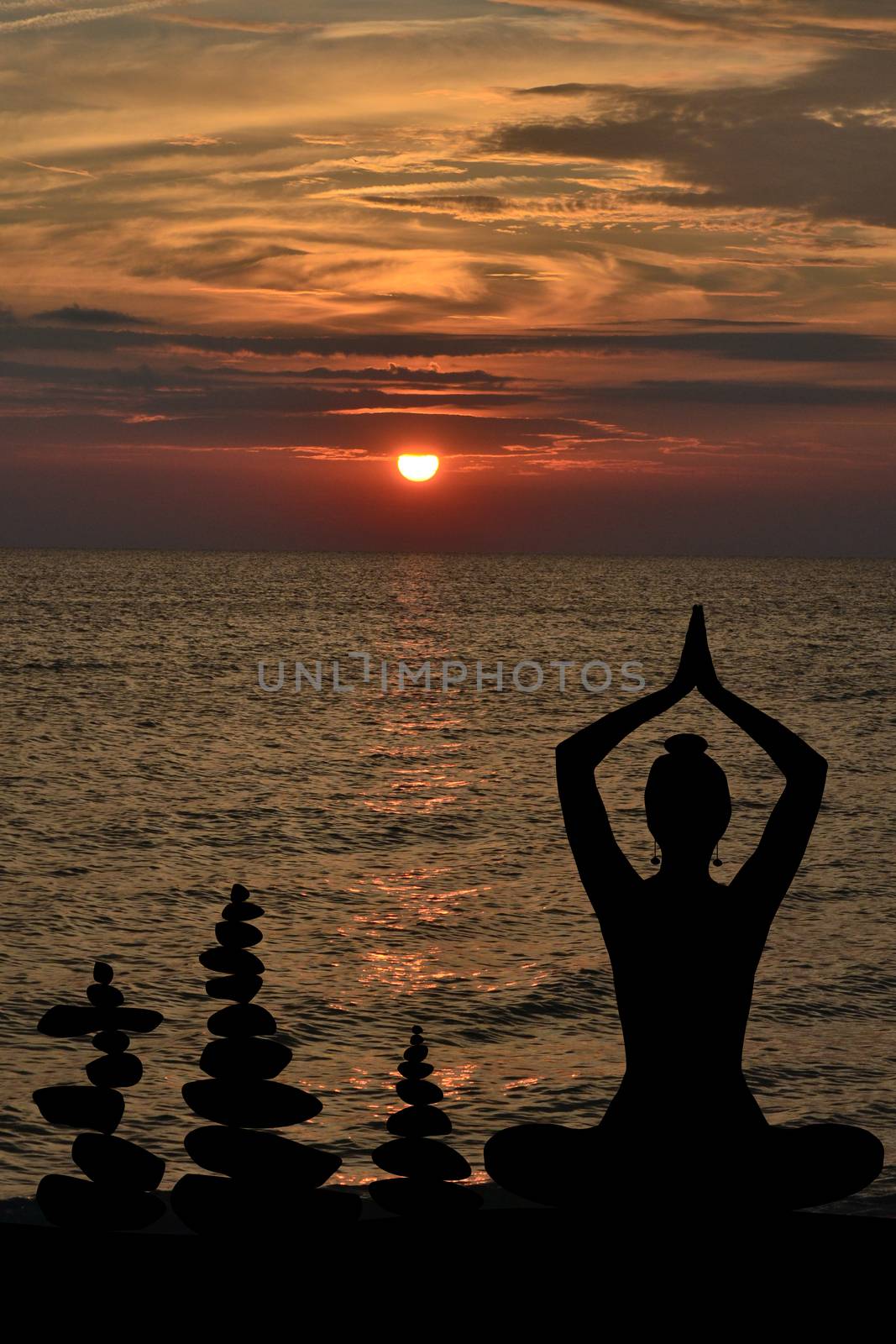 Silhouette of woman in yoga posture and balanced stones at sunrise