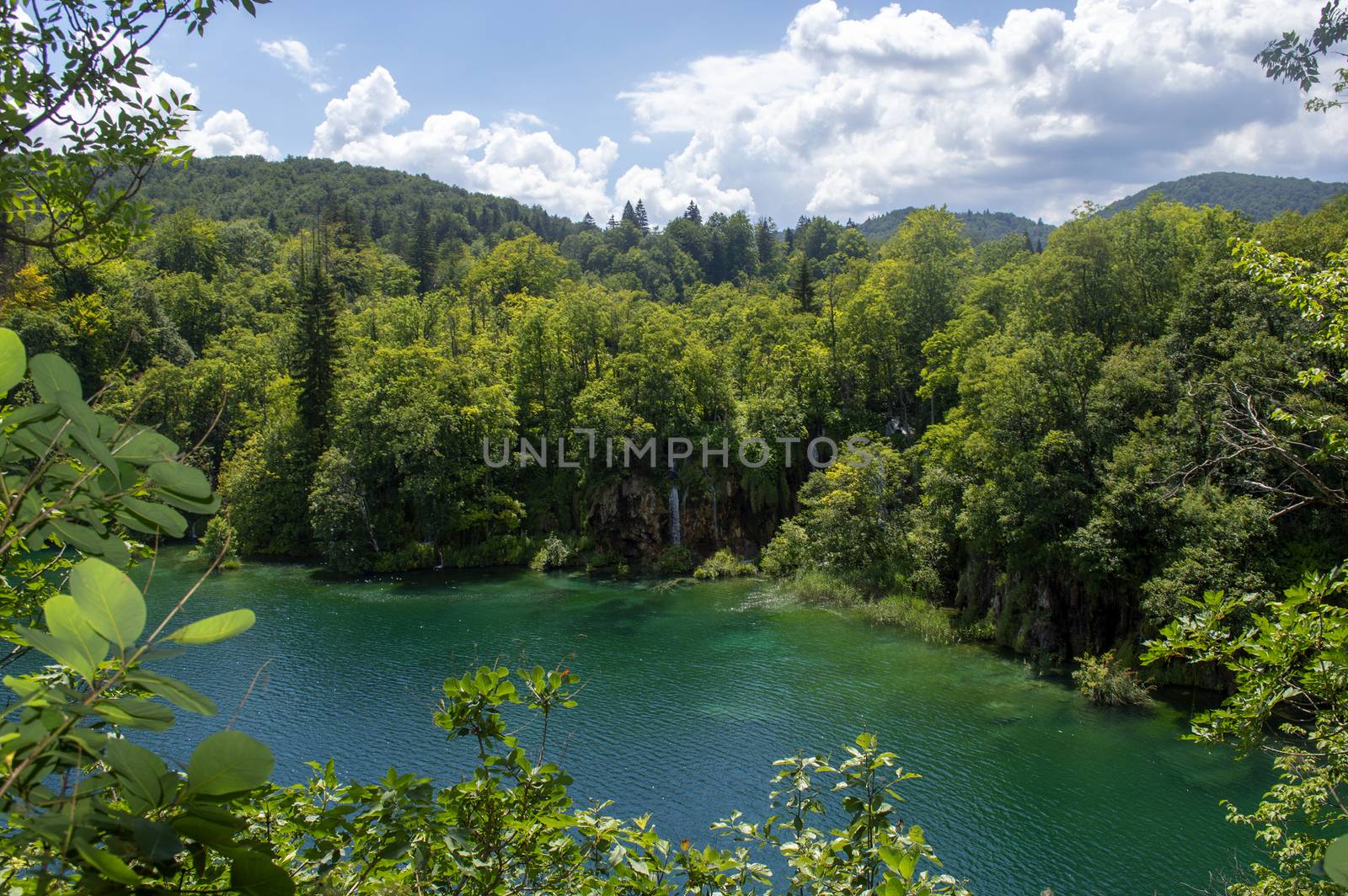 Landscape in Plitvice with green trees, a blue lake and a blue sky with clouds on a sunny day.