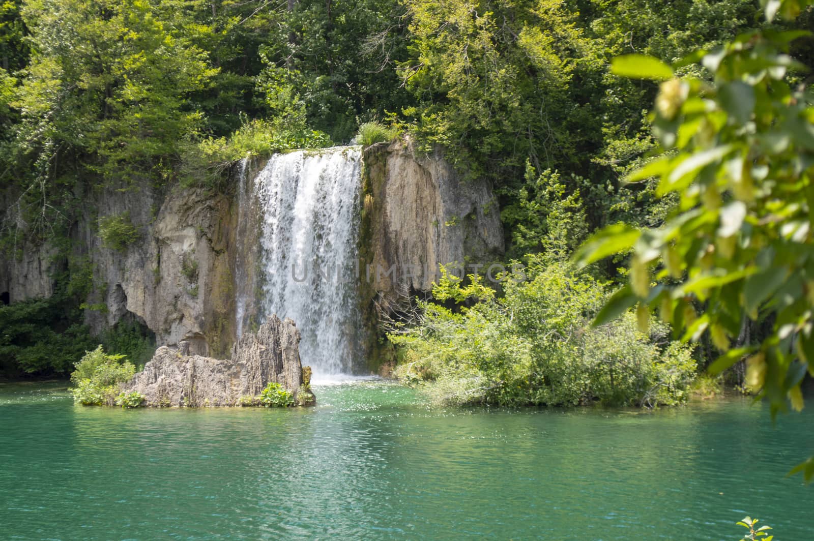 Beautiful waterfall, green trees and a blue lake in Plitvice tourist attraction.