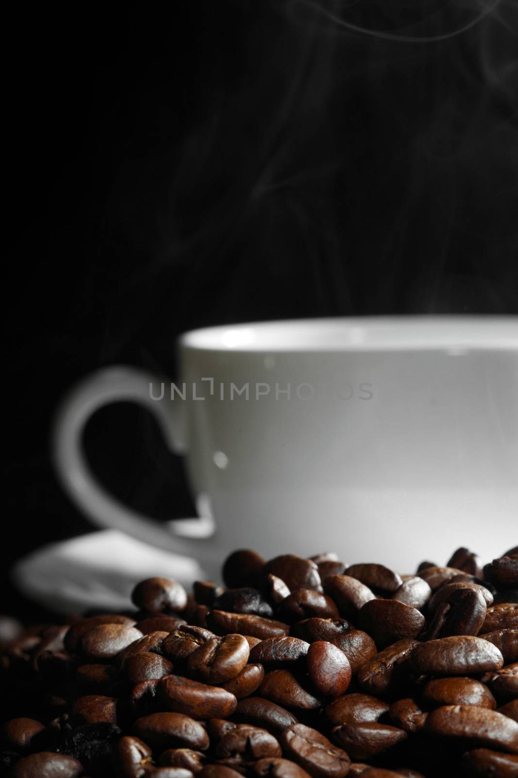 Cup of steaming coffee on coffee beans on black background