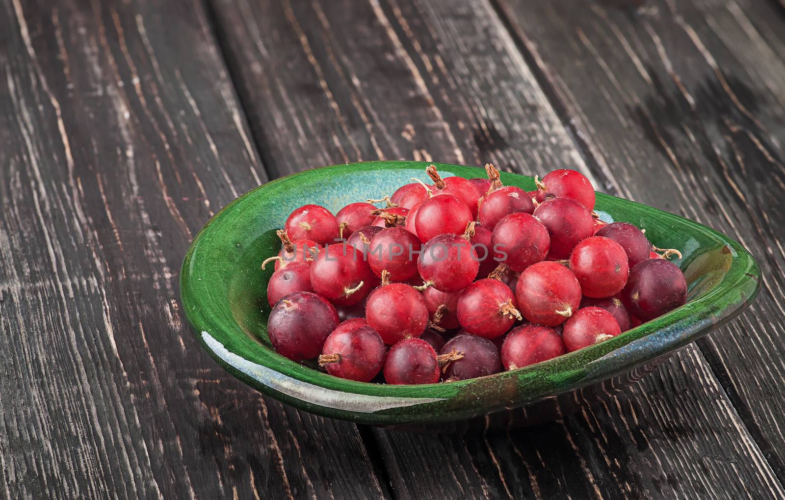 Red gooseberry in clay bowl. Wooden table. Blurred background.