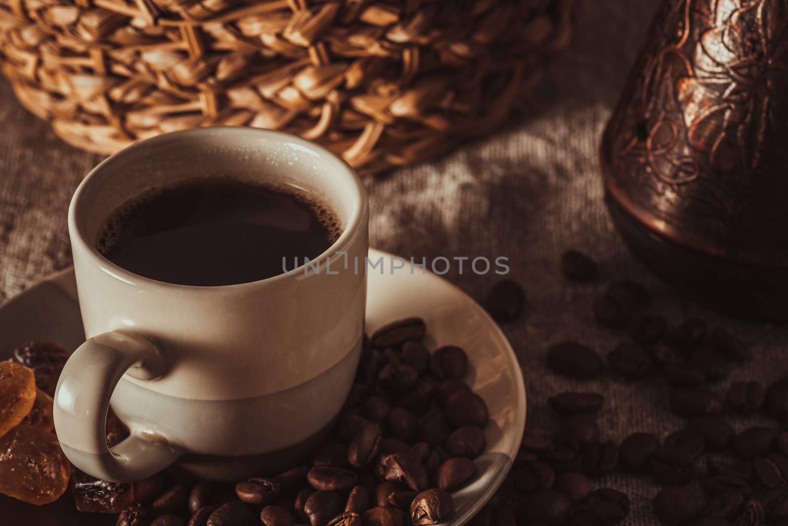 A cup of coffee on textile with coffee beans, dark candy sugar, pots, basket