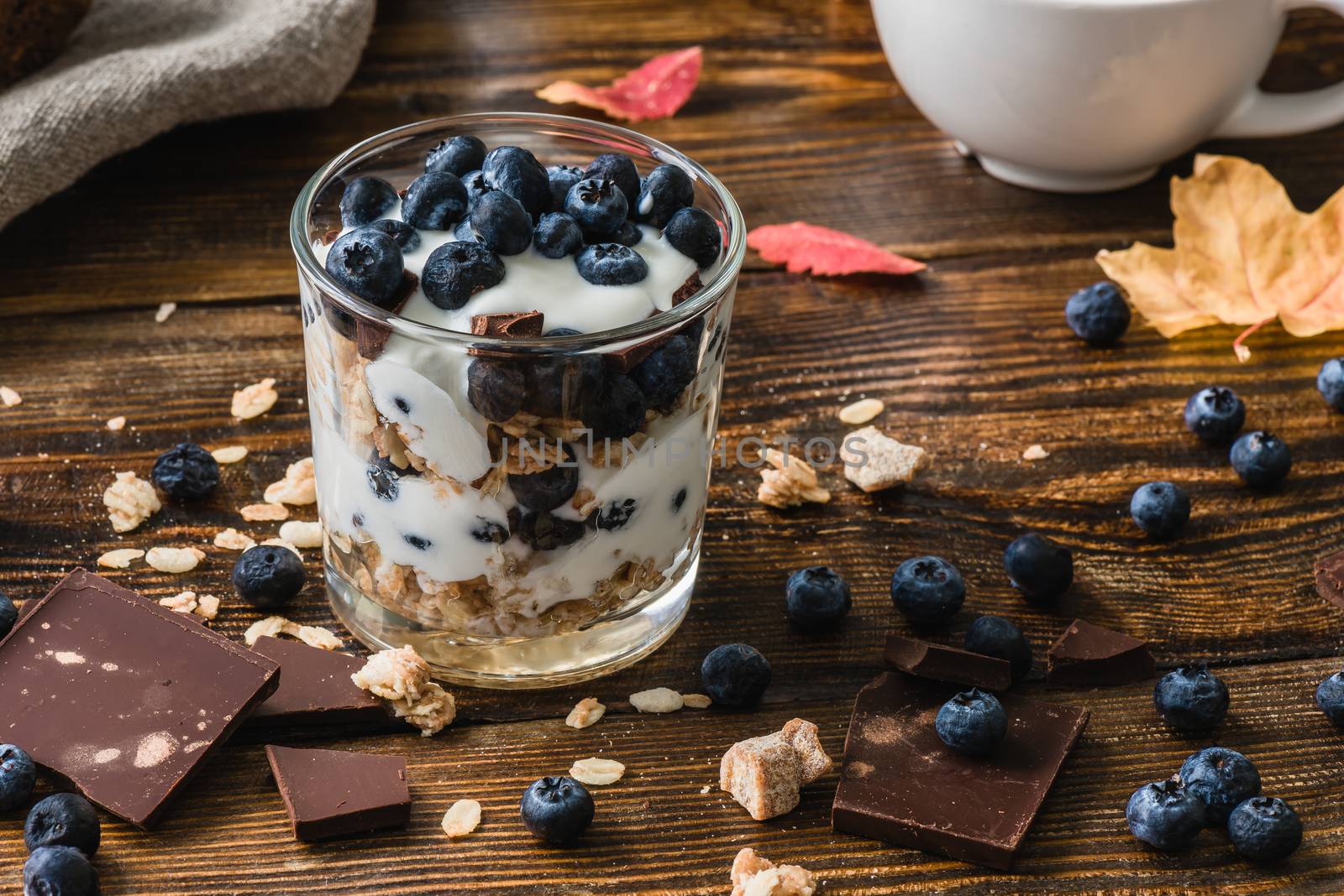 Granola with yogurt, blueberries, honey and chocolate bars on wooden table with ingredients.