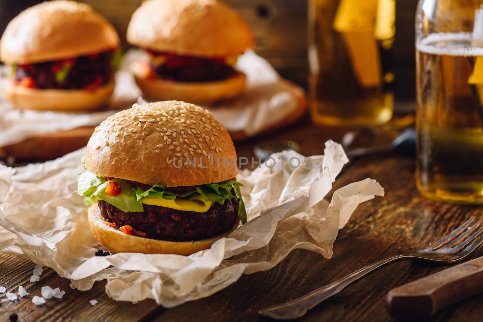 Cheeseburger on Kraft Paper and Some Burgers with Bottles of Beer on Background.