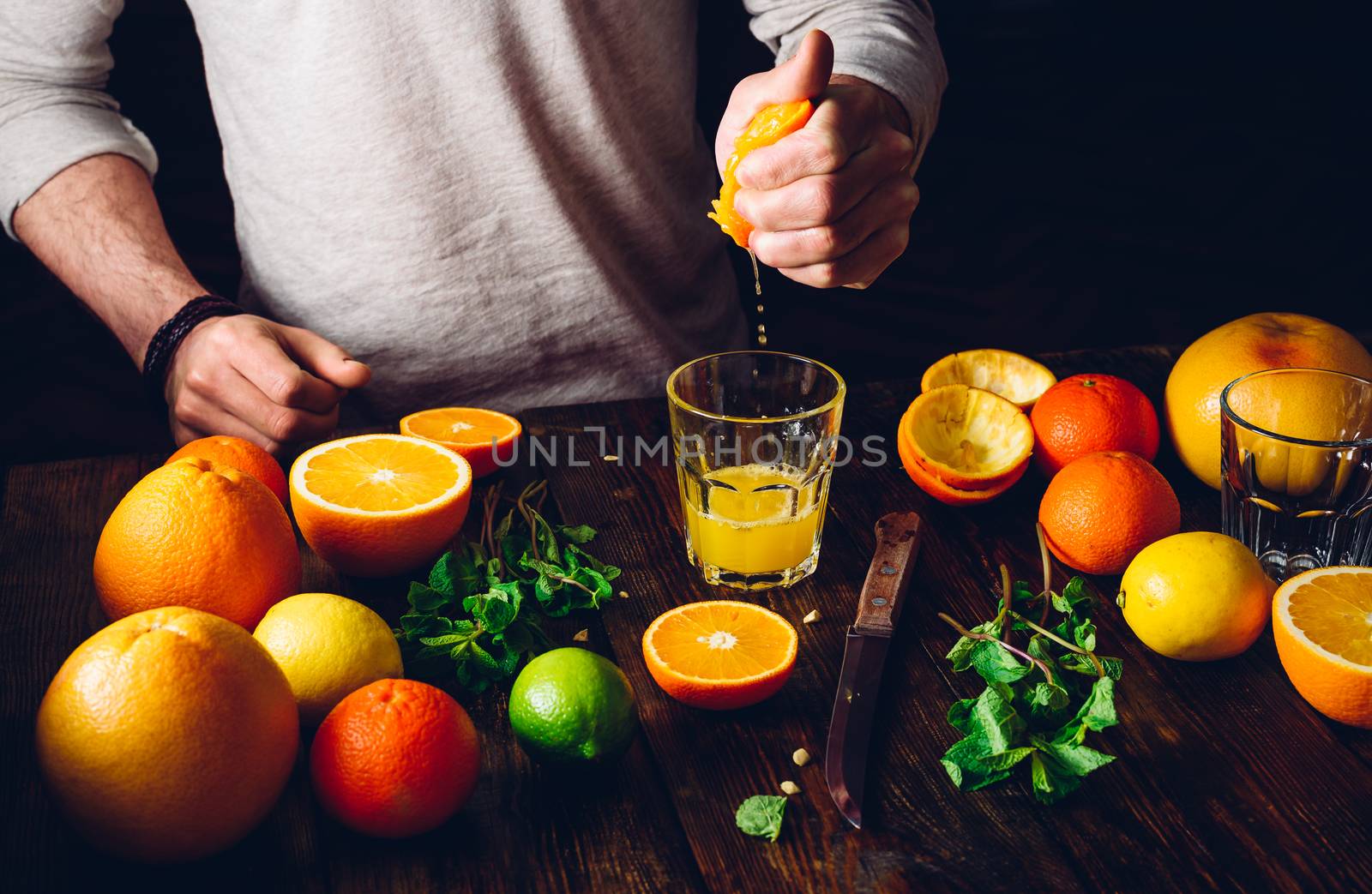 Guy Prepare the Citrus Cocktail. Glass of Juice, Fruits and Mint on Table.